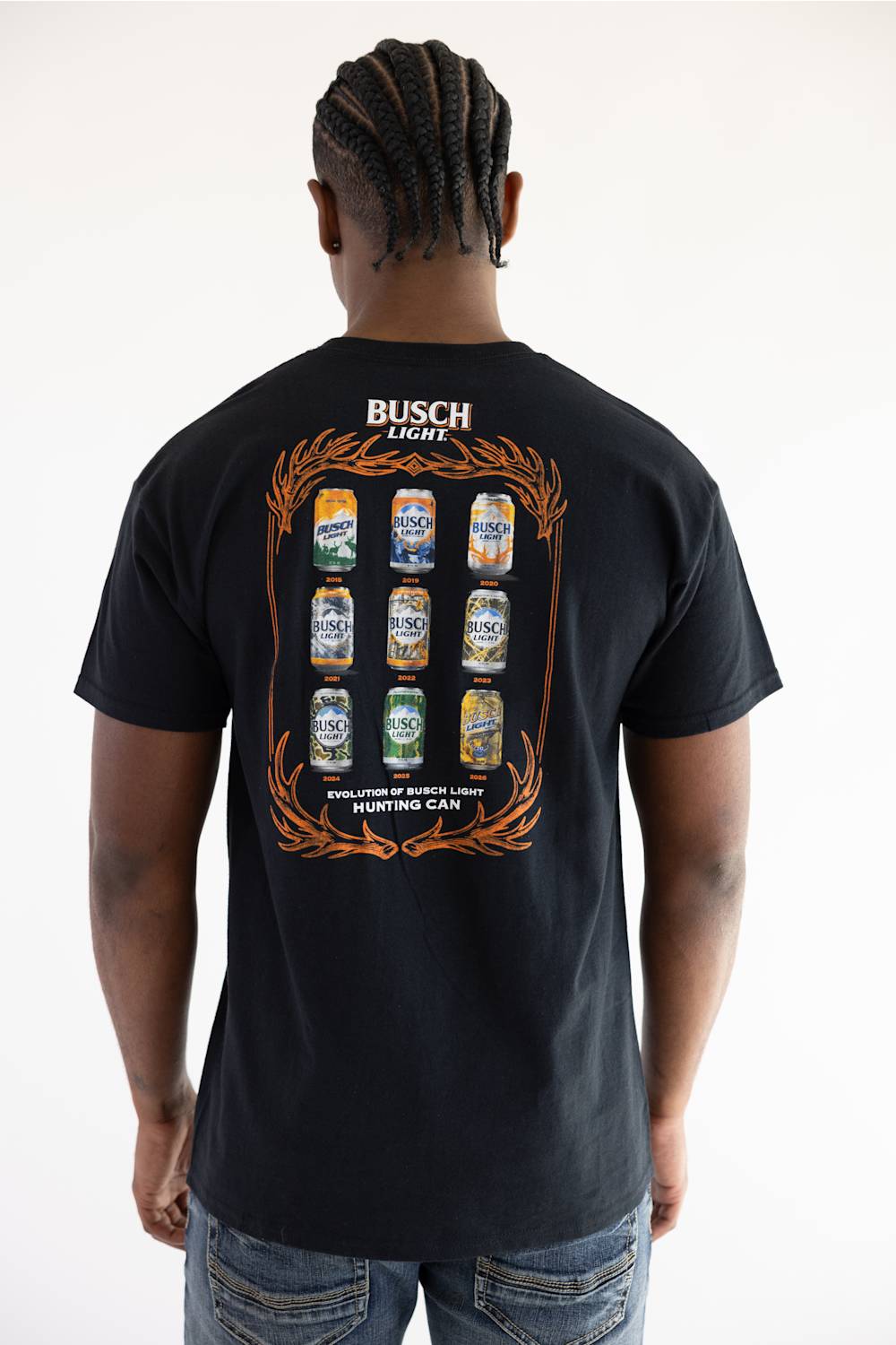 A detailed photograph of the back of a male model with a braided hairstyle, wearing the black Busch Light Can Evolution T-Shirt. The shirt features a large graphic design on the back including nine vintage Busch Light hunting cans arranged chronologically from 2015 to 2026, framed by an orange antler design, and the text 'EVOLUTION OF BUSCH LIGHT HUNTING CAN'.