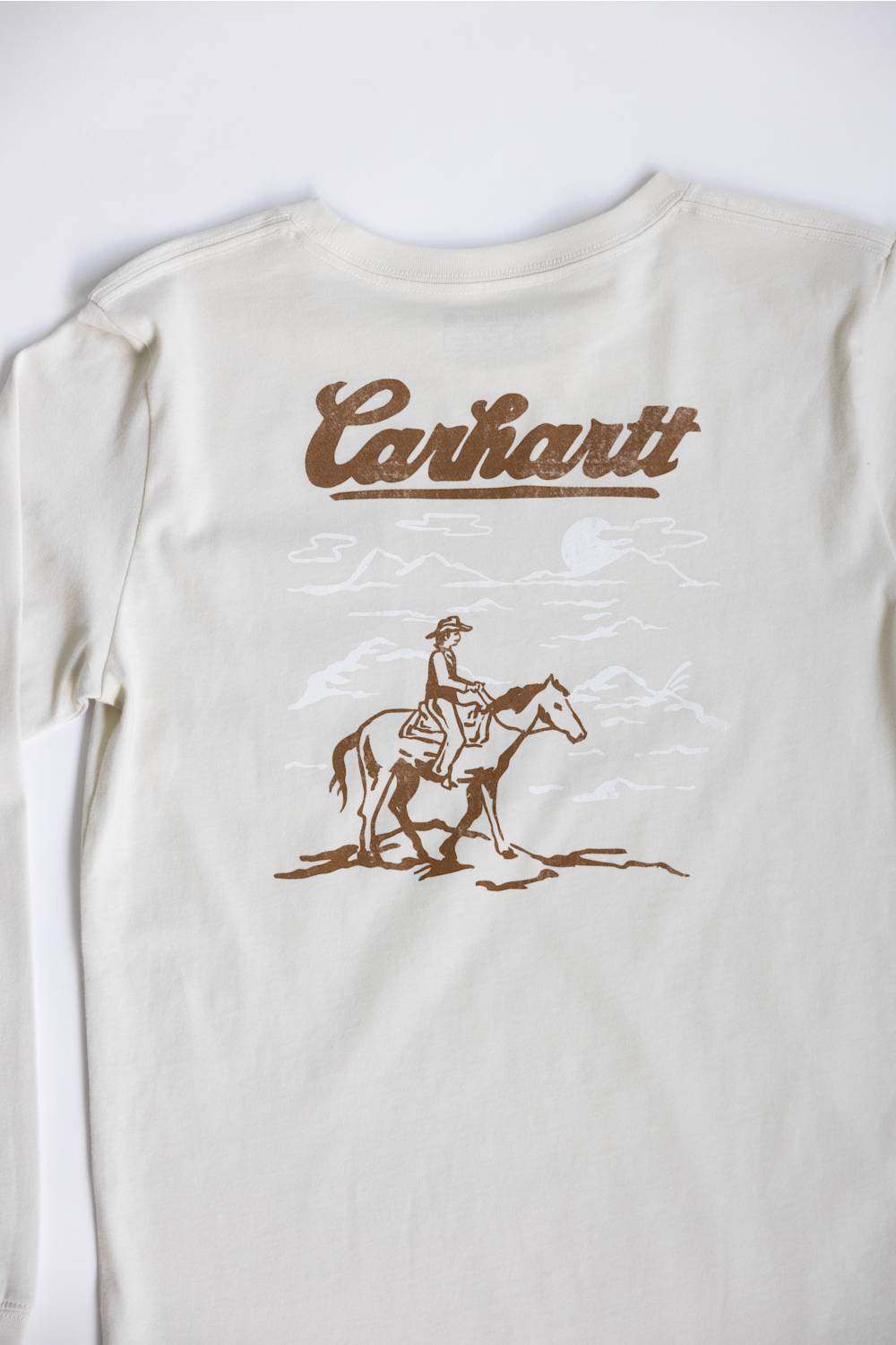 An off-white Carhartt long-sleeve t-shirt featuring a brown graphic print of a cowboy riding a horse beneath the Carhartt logo, displayed flat against a light background.