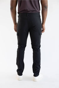 Rear view of a person wearing black cargo pants, a dark brown t-shirt, and white sneakers against a plain white studio background.