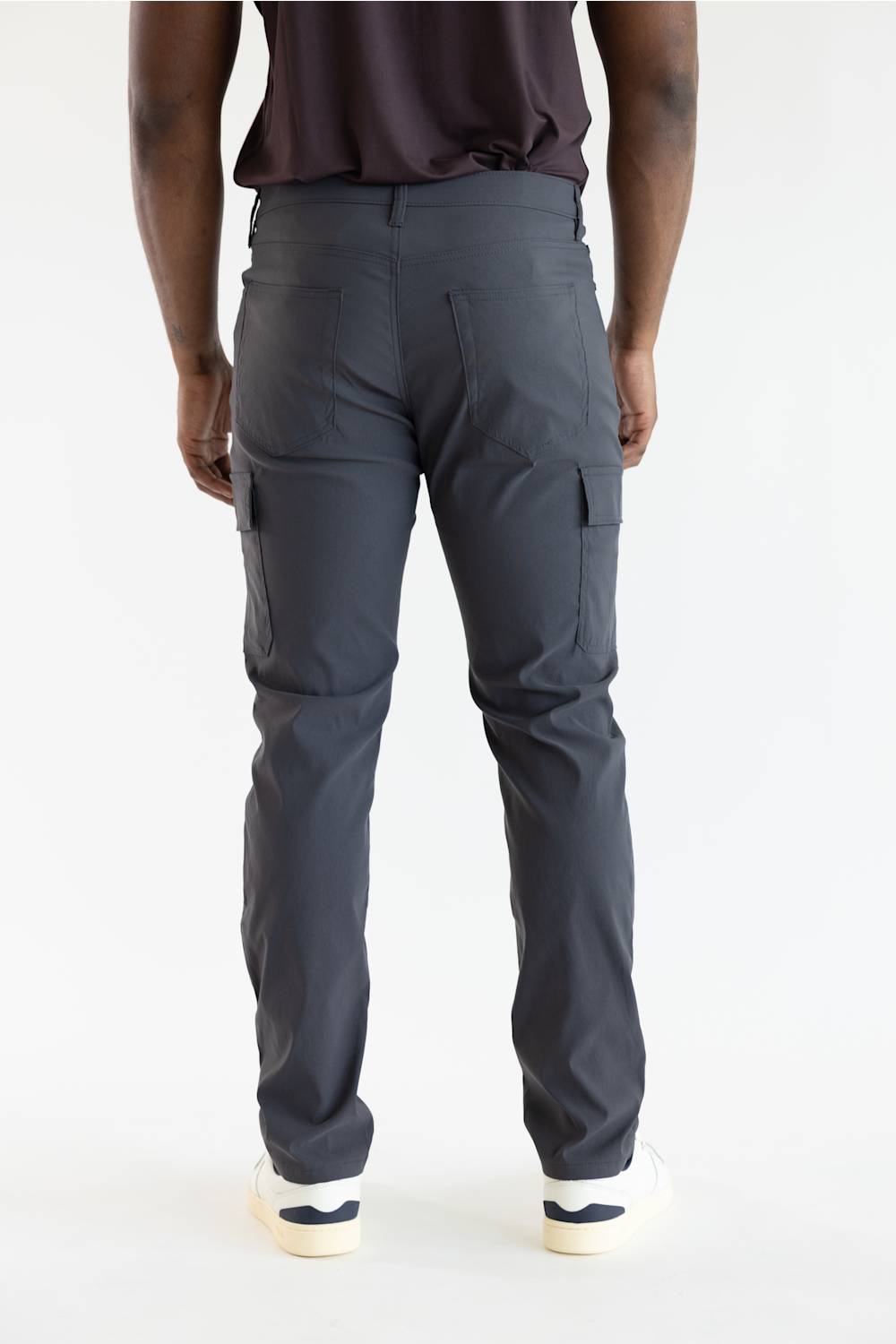 Rear view of a person wearing dark charcoal cargo pants with a dark brown top and white sneakers, photographed against a clean white studio background.