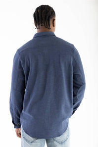 A man viewed from behind wearing a navy blue long-sleeve button-up shirt and light wash jeans against a plain white background.