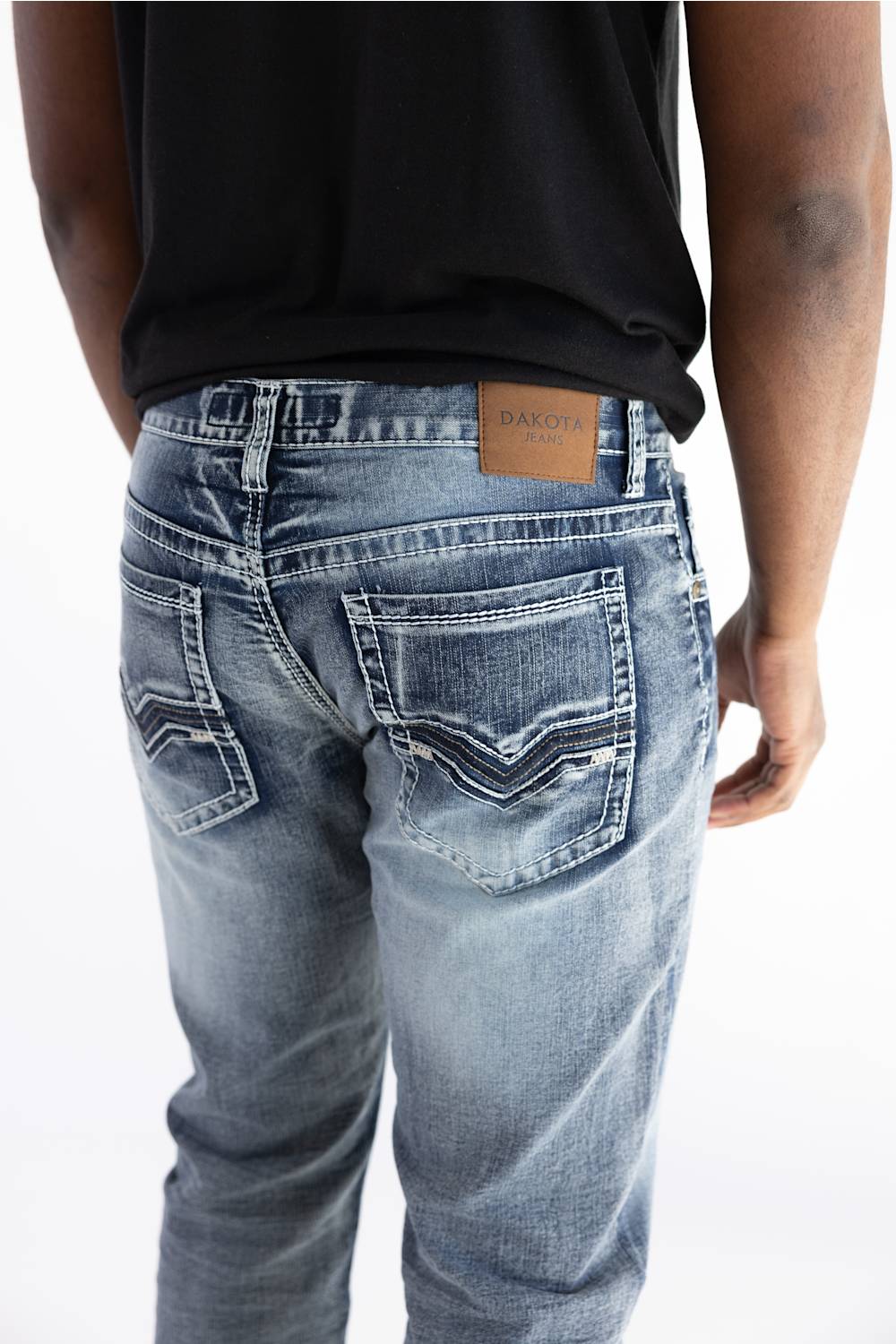 Rear view of a person wearing light-wash blue denim jeans with a black shirt, showing the back pockets and a brown leather brand patch that reads BAKERY.