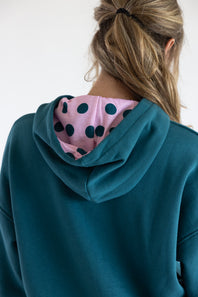A person shown from the back wearing a teal hoodie with a pink hood lining featuring black polka dots.