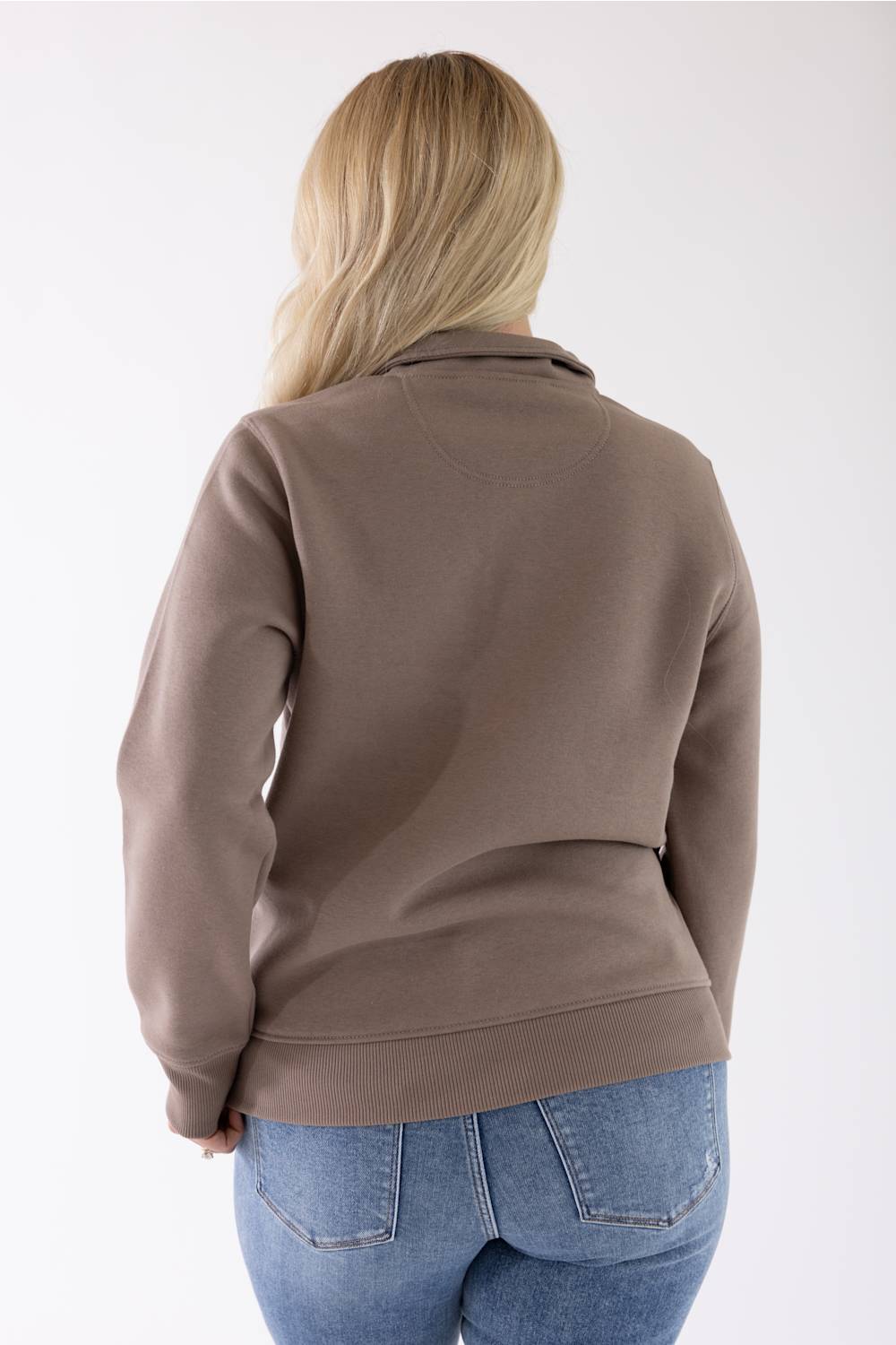 Back view of a stone brown Carhartt quarter-zip sweatshirt featuring a mock-neck collar and rib-knit cuffs, worn with blue jeans against a neutral background.