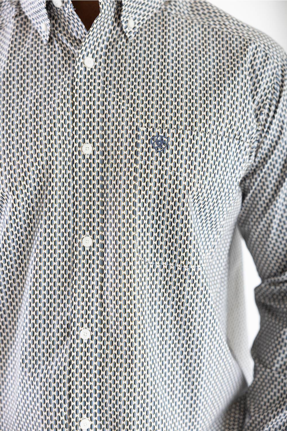 Close-up of a men's long-sleeve button-down shirt with a small-scale geometric pattern in gray and white, featuring white buttons and a small embroidered logo on the left chest.