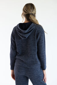 A woman viewed from behind wearing a dark heathered navy ribbed knit hooded sweatshirt and matching pants against a plain white studio background.