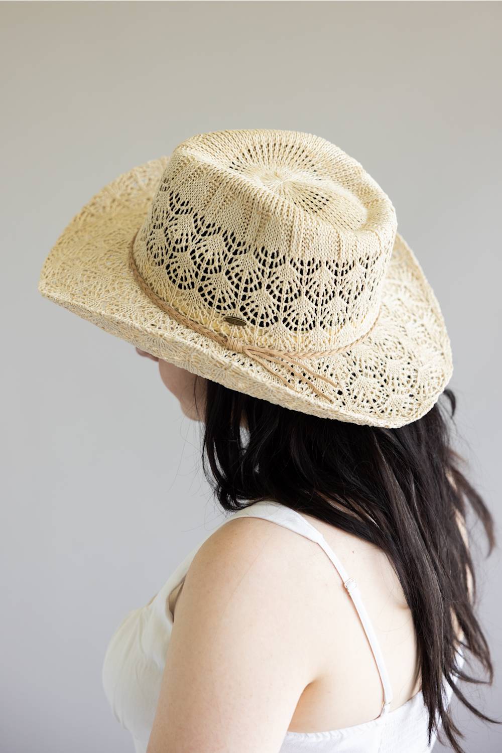 Person wearing a beige straw hat with a subtle pattern on a plain background