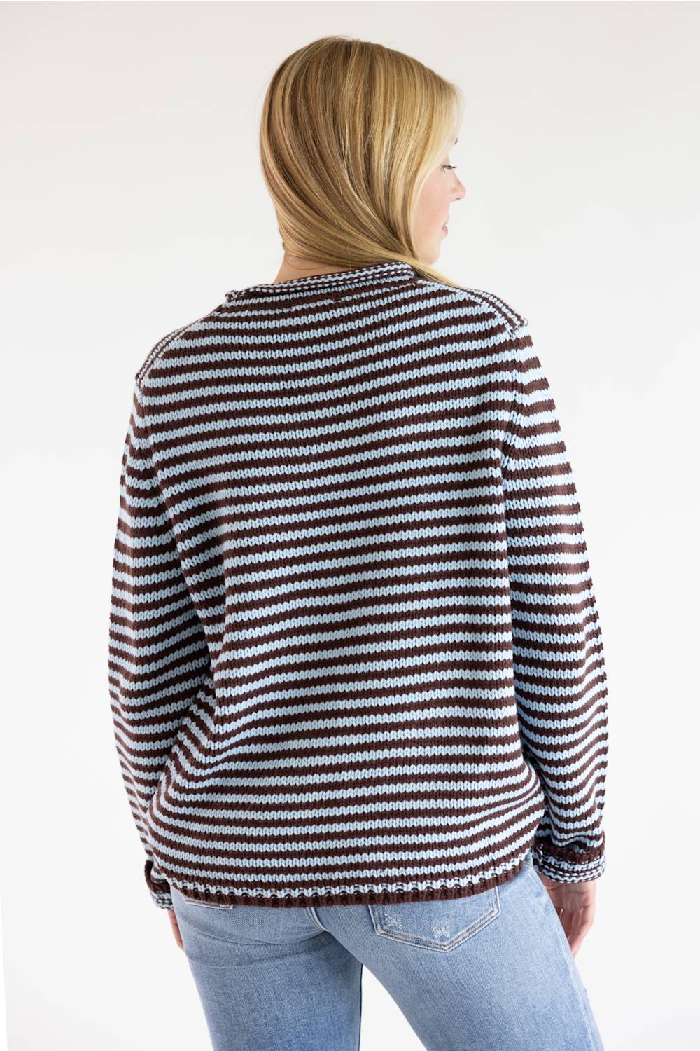 A woman shown from the back wearing a brown and white horizontally striped knit sweater and light blue jeans against a plain white studio background.