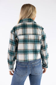 A woman viewed from the back wearing a green and white plaid flannel shirt and blue jeans against a plain white background.