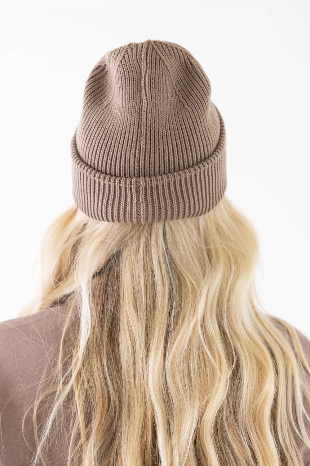 rear view showing the ribbed knit texture of the stone brown Carhartt watch cap beanie worn over blonde hair.