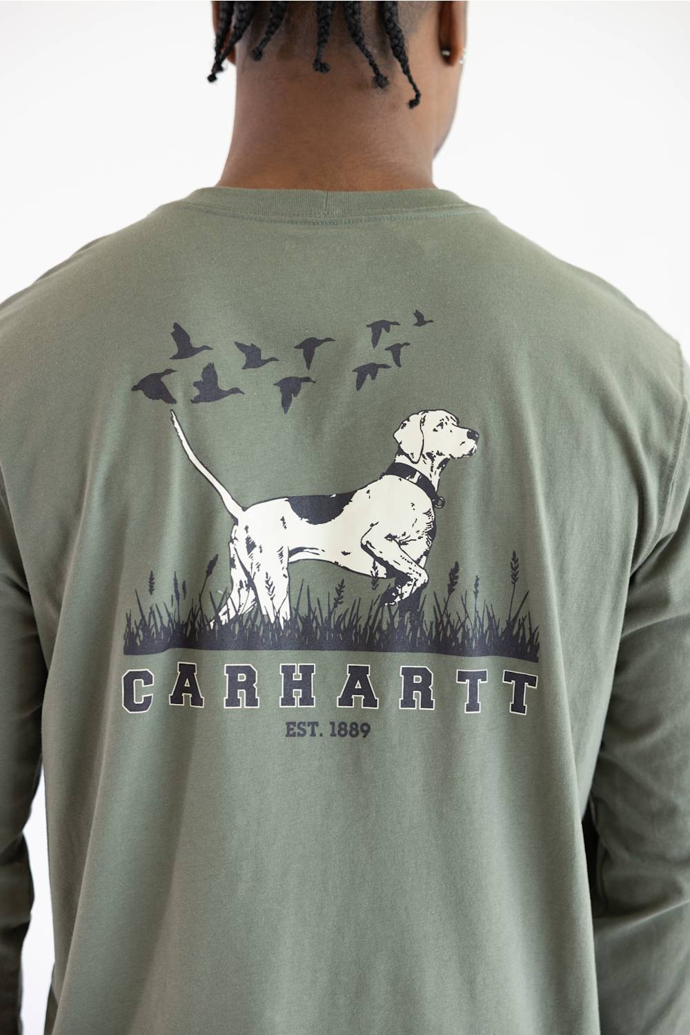 A close up of a man from the back wearing the Carhartt Irvine Relaxed Pointer Dog Long Sleeve T-Shirt for Men in Dusty Olive Green featuring a Carhartt logo down the left arm and pointer dog logo with birds on the back.
