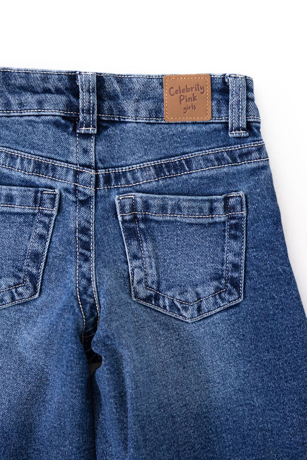 Close-up back view of Celebrity Pink youth girls' medium wash denim jeans highlighting the back pockets, waistband, and brown "Celebrity Pink girls" brand patch.