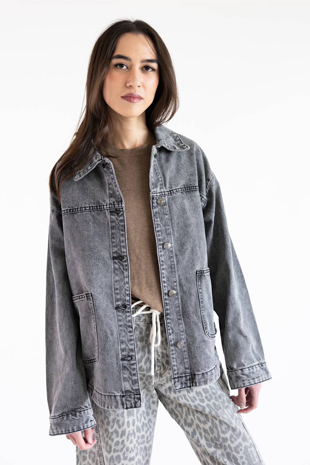 A woman modeling a washed gray denim jacket over a brown top and leopard-print pants against a plain white background.
