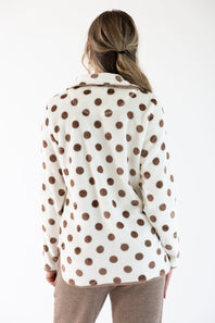 A woman viewed from behind wearing a cream-colored fleece jacket with brown polka dots and brown corduroy pants, set against a plain white background.
