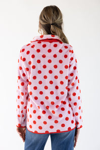 A woman viewed from behind wearing a light pink fleece jacket with a bold red polka dot pattern and red trim, paired with blue jeans against a plain white background.