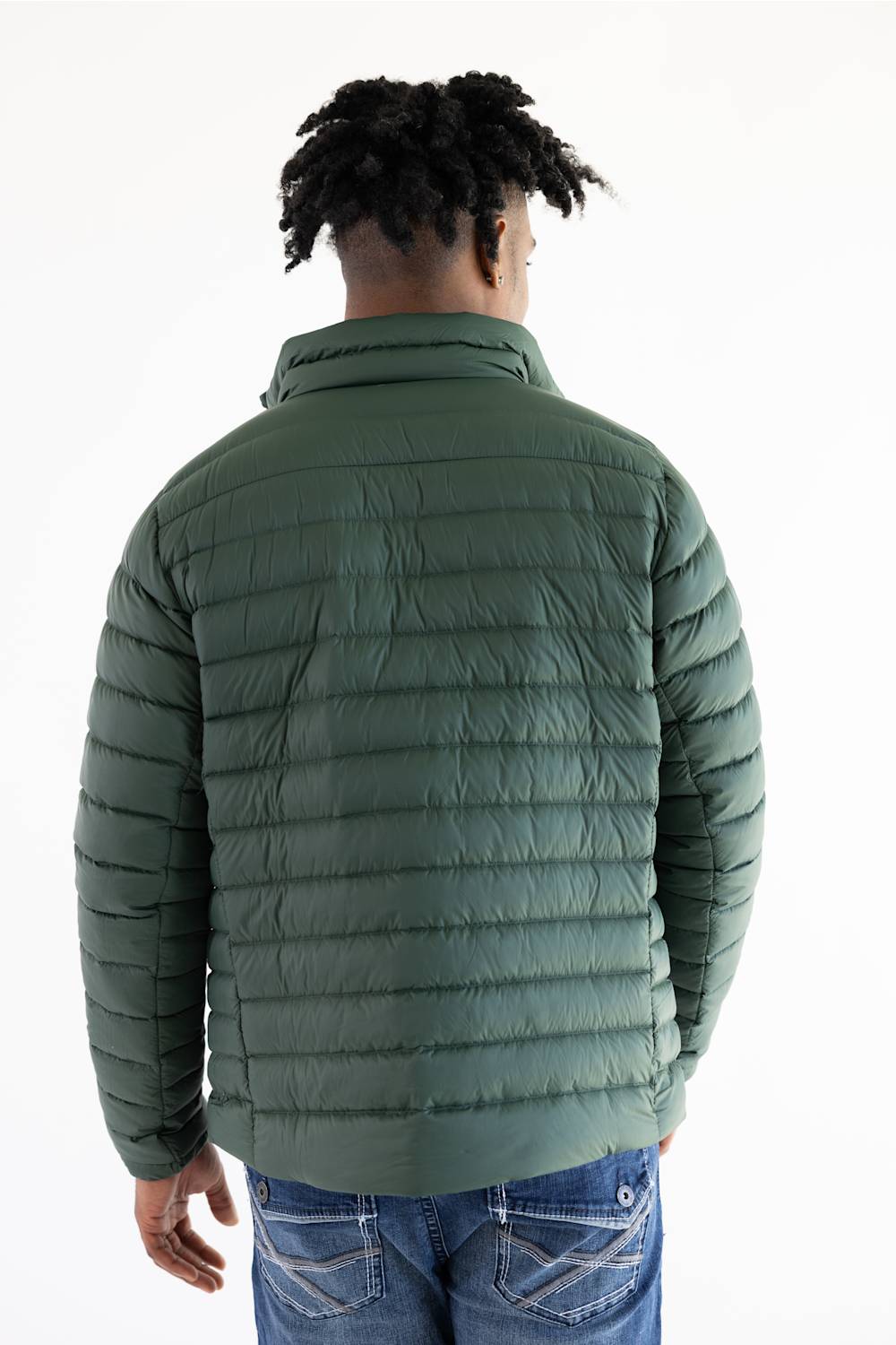 A man viewed from behind wearing an olive green quilted puffer jacket and blue jeans against a plain white background.