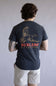 Back view of a person wearing a navy t-shirt with a bird graphic and 'Burlebo Outdoors' text on the back, standing against a plain background. The shirt is Burlebo Duck Wild Tee for Men in Heather Black