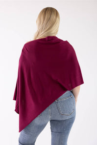 A woman viewed from behind wearing a deep burgundy draped wrap or poncho over light blue jeans, set against a plain white studio background.