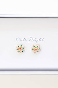 A pair of gold-toned floral stud earrings with green and red stones, displayed on a white card labeled 'Date Night' inside a white box.