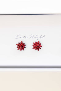 A pair of small red flower-shaped stud earrings displayed on a white card that reads 'Date Night'.