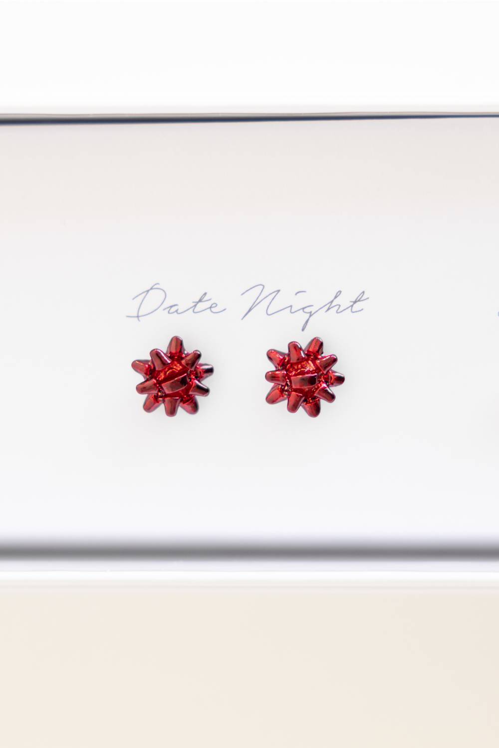 A pair of small red flower-shaped stud earrings displayed on a white card that reads 'Date Night'.