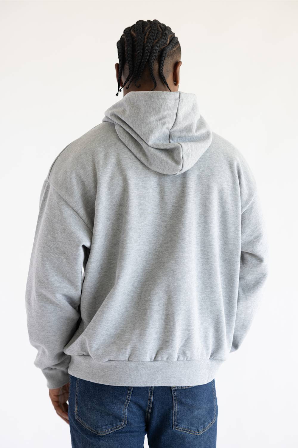 A person viewed from the back wearing a light gray oversized hoodie and blue jeans against a plain white background.