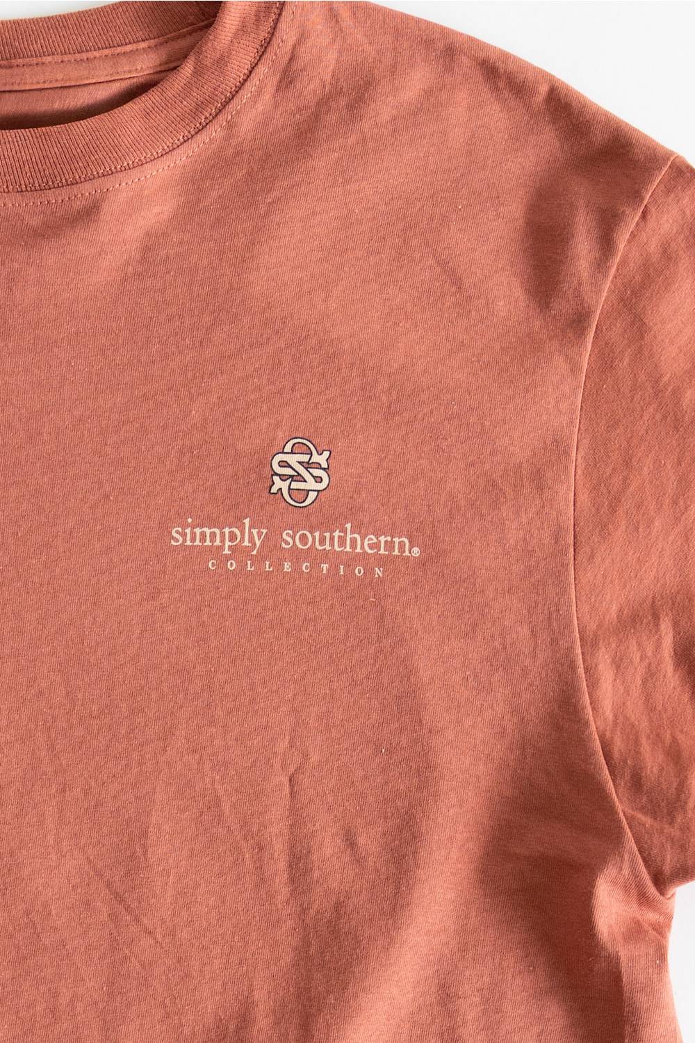 A close-up of a dusty rose crewneck t-shirt featuring a white embroidered logo and 'simply southern COLLECTION' text on the left chest.