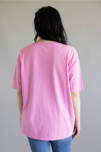 A person viewed from the back wearing a light pink short-sleeve t-shirt and blue jeans, standing against a plain light gray wall.