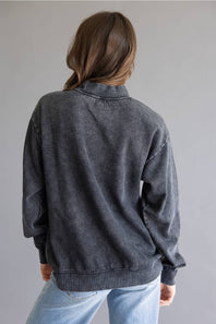 A person viewed from the back wearing a dark charcoal gray washed sweatshirt and light blue jeans against a plain gray background.