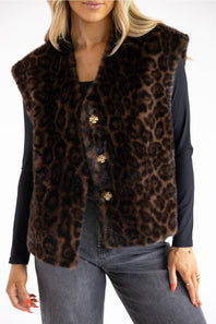 A woman wearing a brown and black leopard-print faux fur vest with gold-tone buttons over a black long-sleeve top and gray jeans.