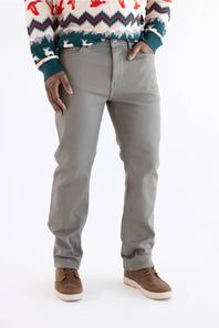 A person wearing light gray slim-fit jeans, a colorful patterned knit sweater, and brown suede shoes, standing against a plain white studio background.