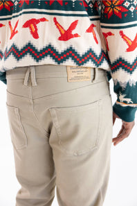 Close-up back view of a person wearing light beige chino pants and a festive Christmas sweater with red, green, and white patterns. A tan leather patch on the back waistband shows the brand 'Buckeye Creek'.