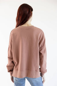 A person shown from the back wearing a dusty rose crewneck sweatshirt and light blue jeans against a plain white background.