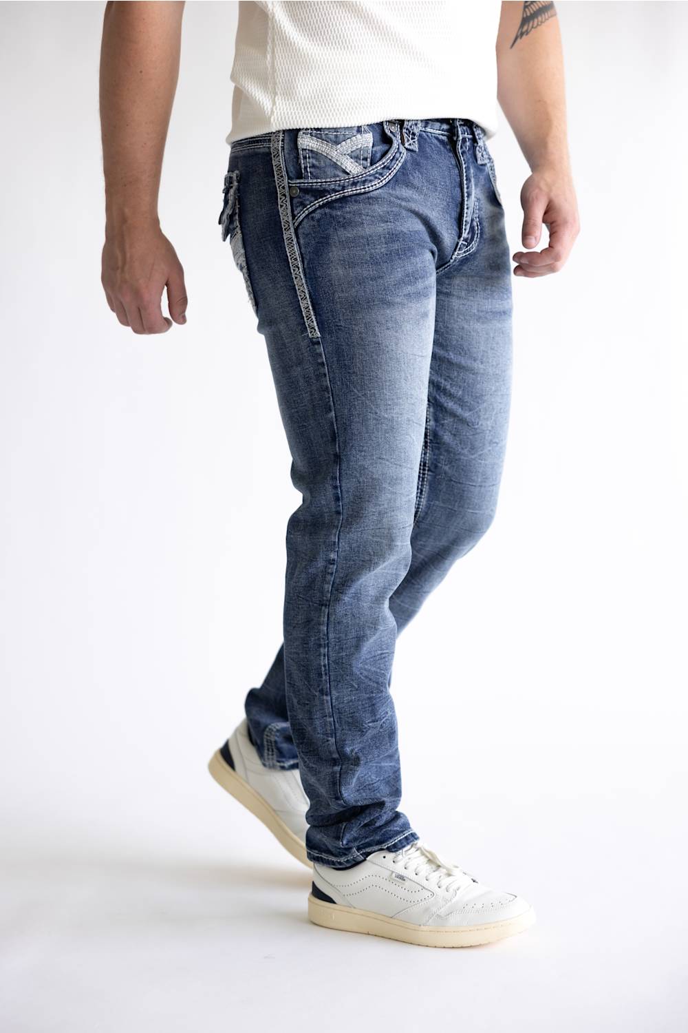 A person wearing blue denim jeans with white sneakers, shown from the waist down against a plain white studio background.