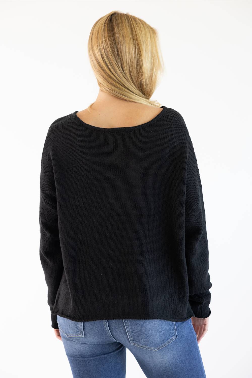 A woman viewed from behind wearing a black long-sleeve knit sweater and blue jeans against a plain white studio background.
