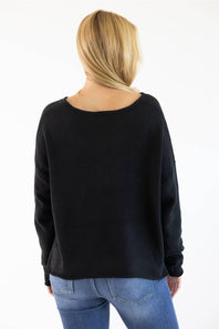 A woman viewed from behind wearing a black long-sleeve knit sweater and blue jeans against a plain white studio background.