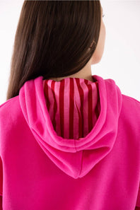 Close-up back view of a person wearing a bright pink hoodie with a striped inner hood lining in red and pink.