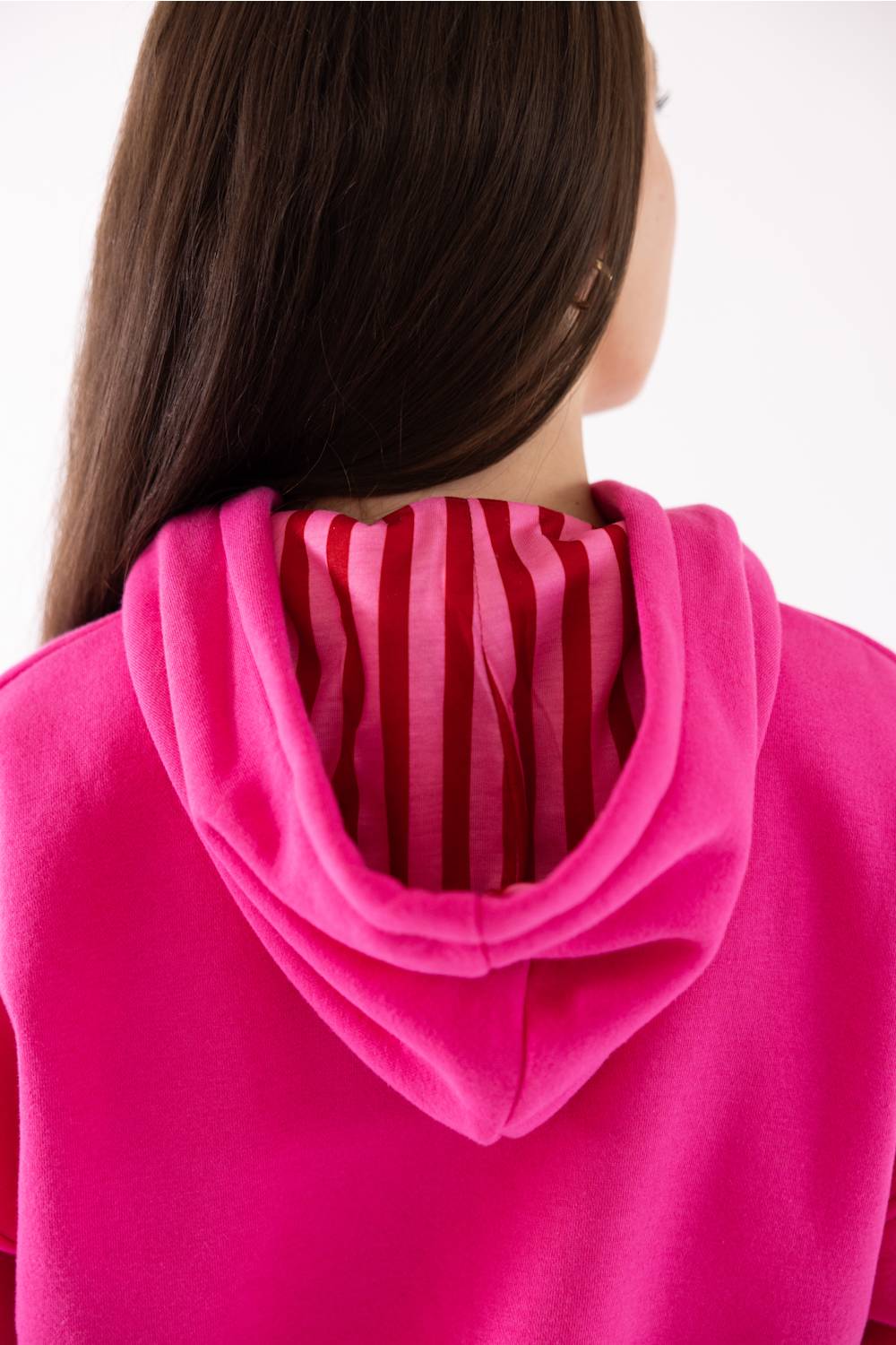 Close-up back view of a person wearing a bright pink hoodie with a striped inner hood lining in red and pink.