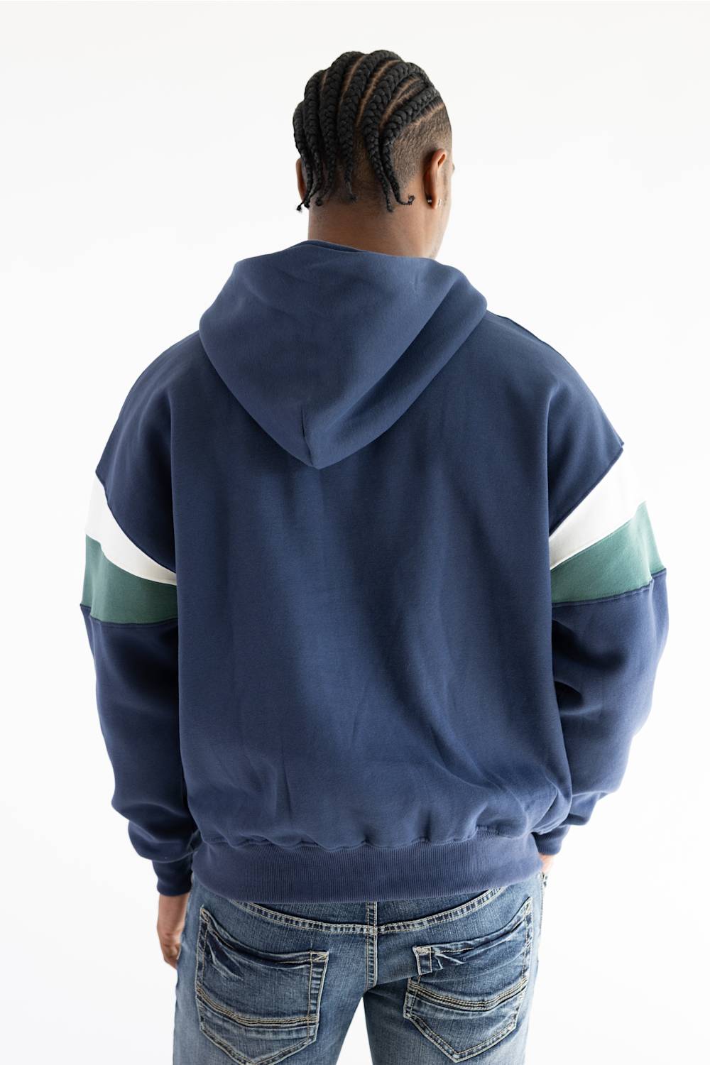 A person viewed from behind wearing a navy blue hoodie with color-blocked sleeves in white and green, paired with blue jeans, against a plain white background.