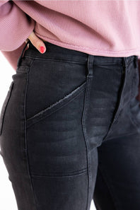 Close-up of a person wearing dark charcoal gray denim jeans with a pink ribbed top, showing the side pocket and waistband details.