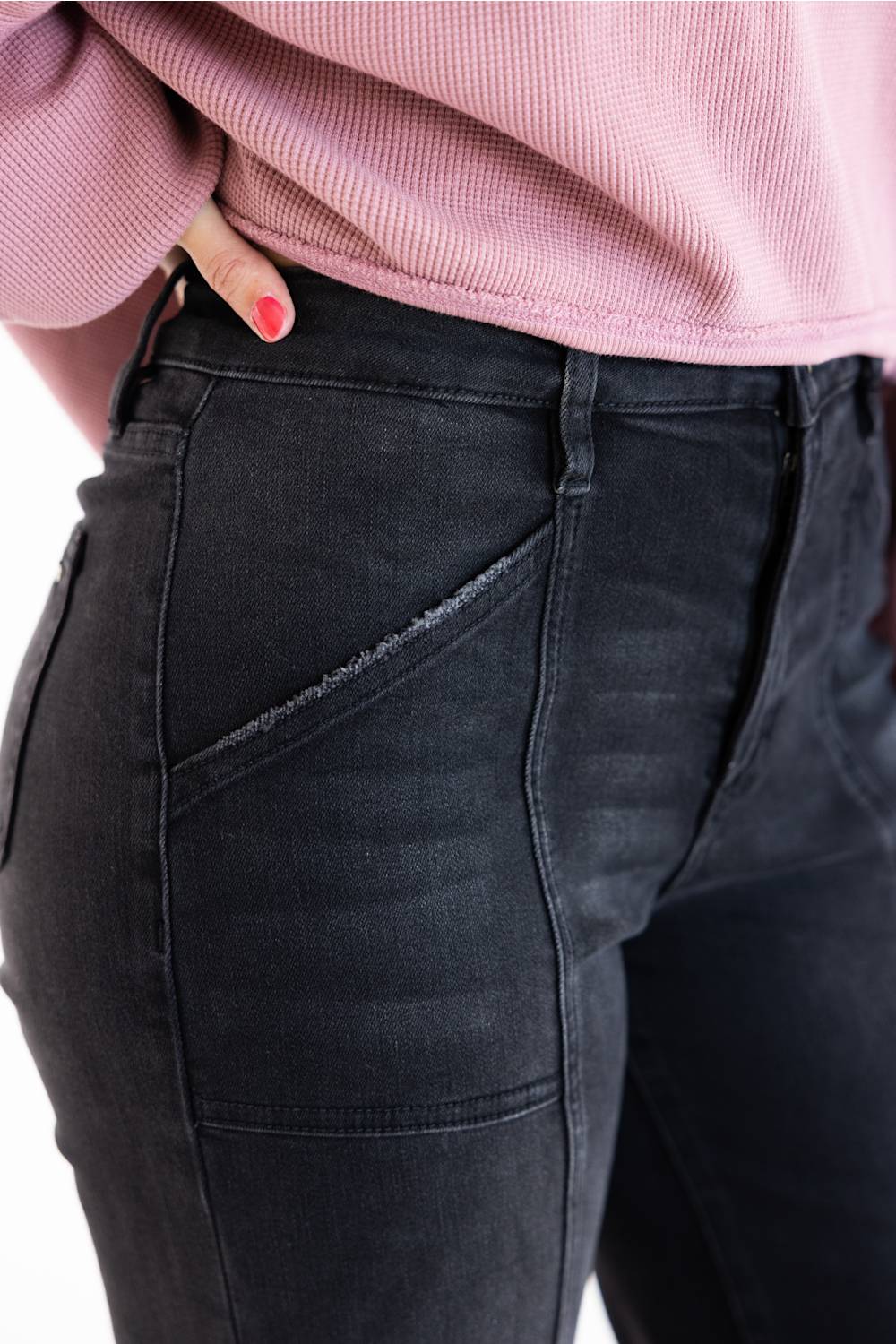Close-up of a person wearing dark charcoal gray denim jeans with a pink ribbed top, showing the side pocket and waistband details.