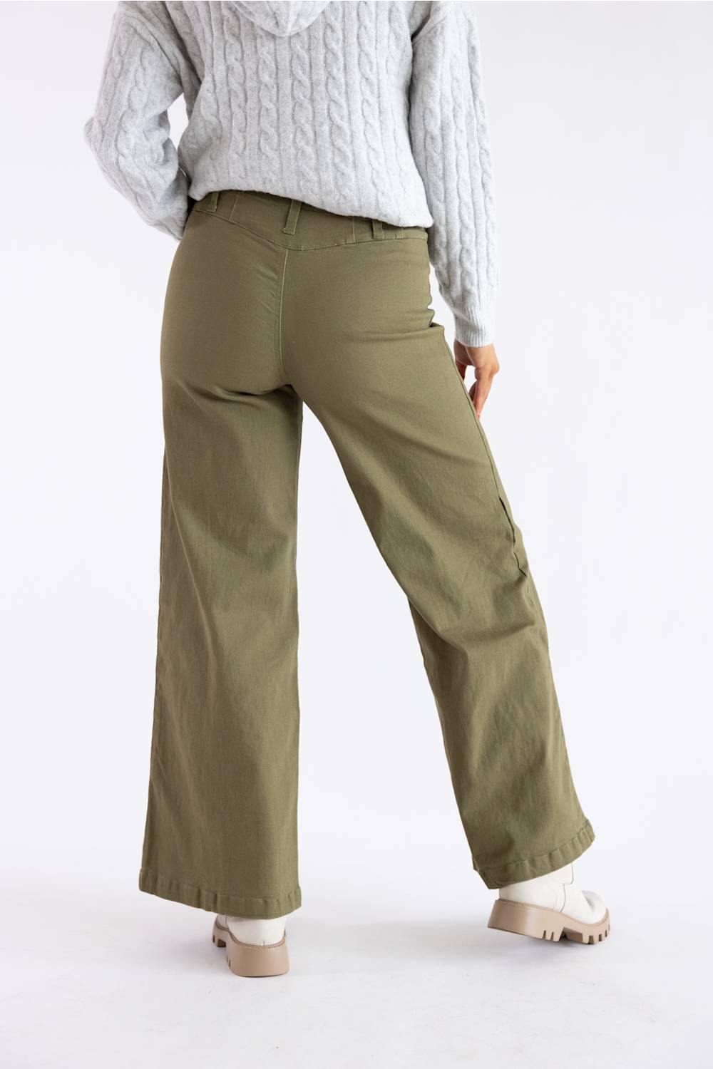 A person shown from the back wearing olive green wide-leg cargo pants, a light gray cable-knit sweater, and beige platform shoes against a plain white studio background.