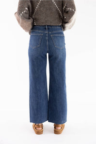 A person shown from the back wearing blue wide-leg jeans, a brown patterned knit sweater, and tan wedge sandals against a plain white studio background.