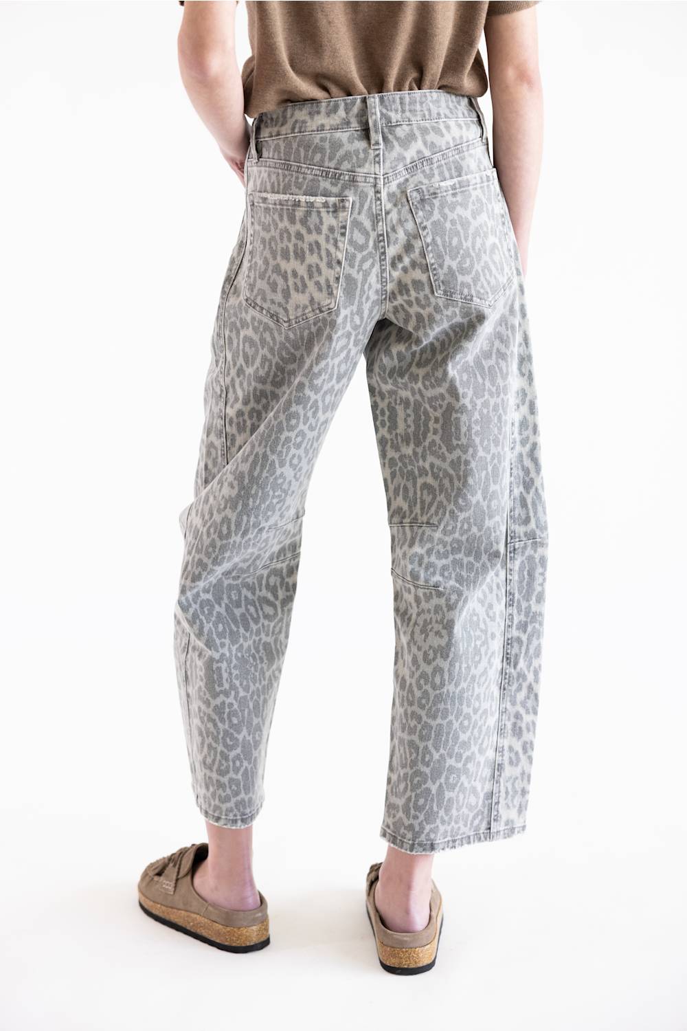 A person shown from the back wearing light gray leopard-print cropped pants, a brown top, and tan slip-on shoes against a plain white studio background.