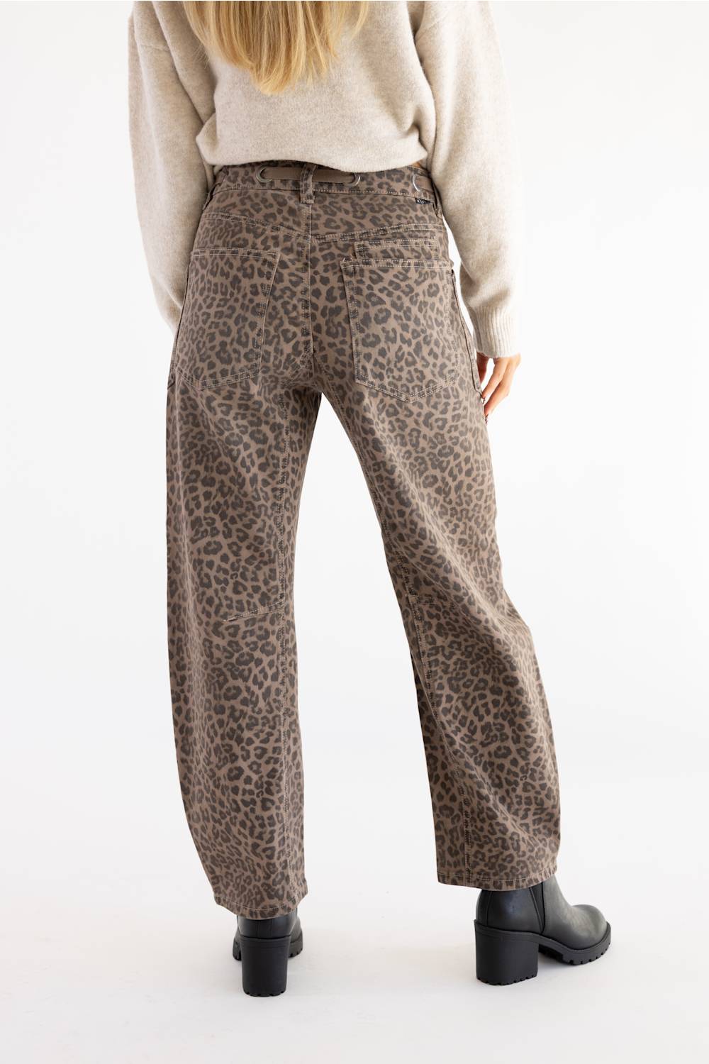back view of woman modeling cheetah print jeans with black boots and tan sweater 