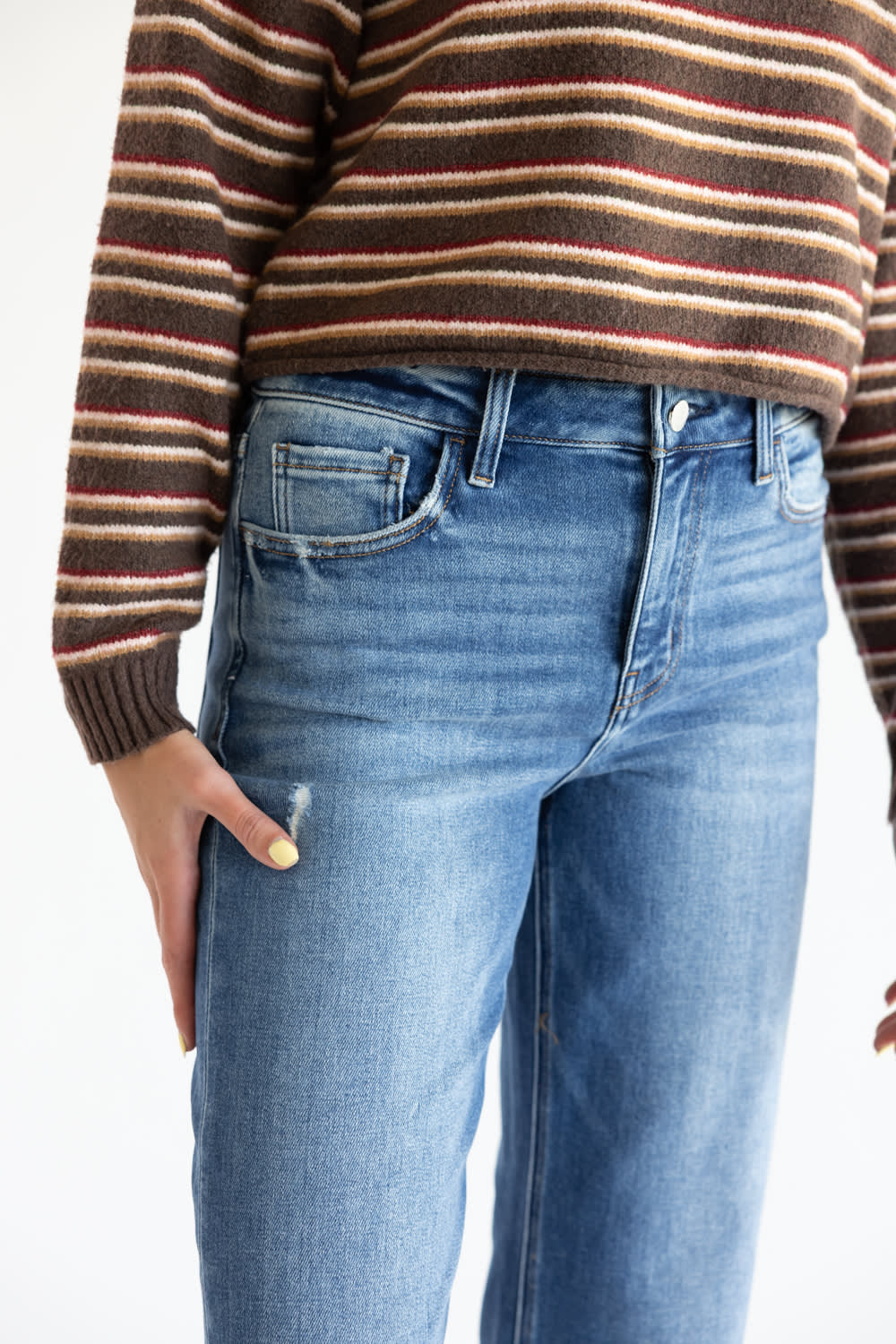 Close-up of a person wearing blue denim jeans and a brown striped sweater against a plain white background.