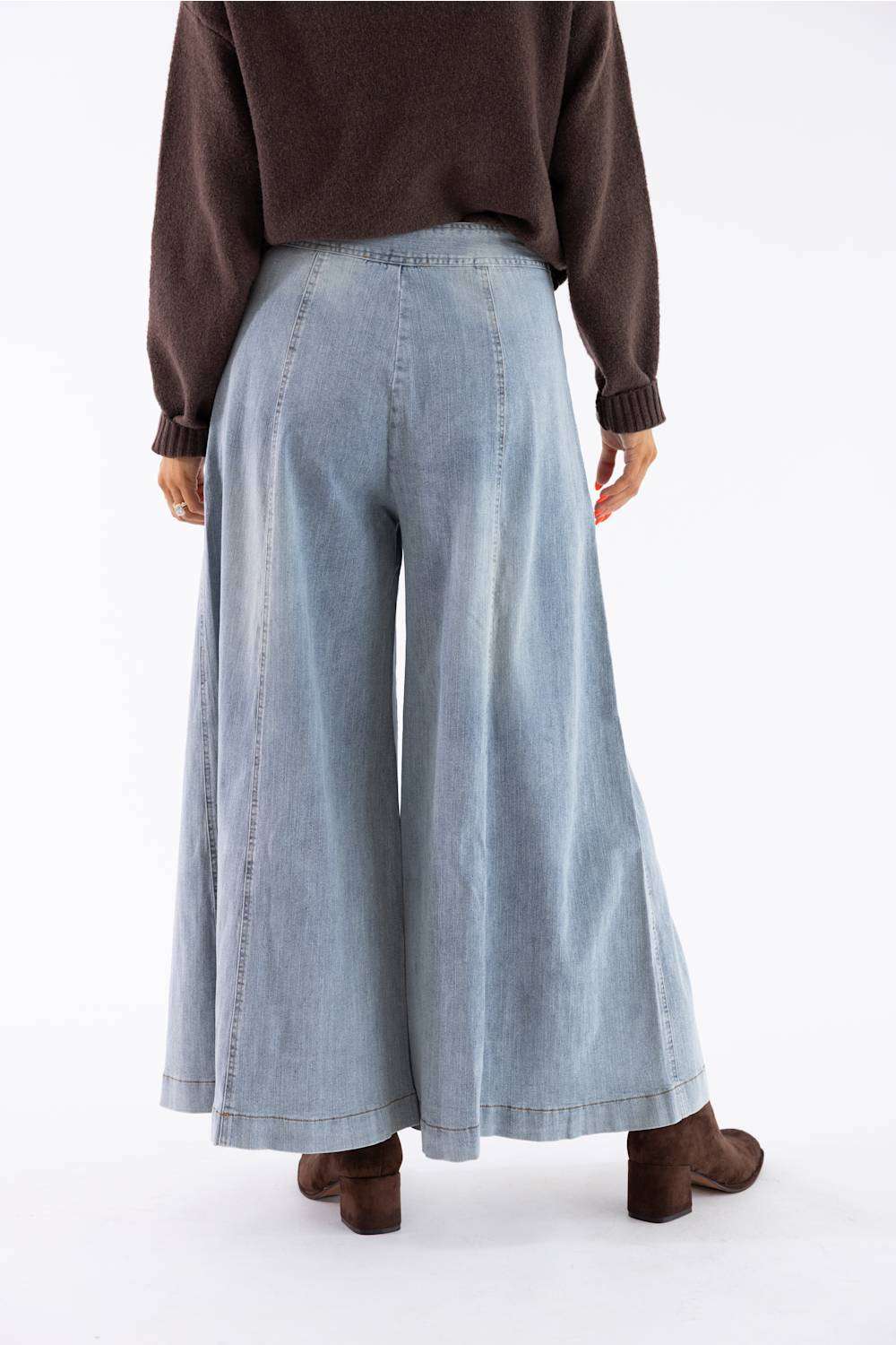A person shown from the back wearing light-wash wide-leg denim pants, a dark brown sweater, and brown boots against a plain white studio background.
