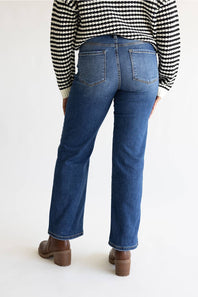 Rear view of a person wearing blue straight-leg jeans, a black and white patterned sweater, and brown block-heel boots against a plain white studio background.