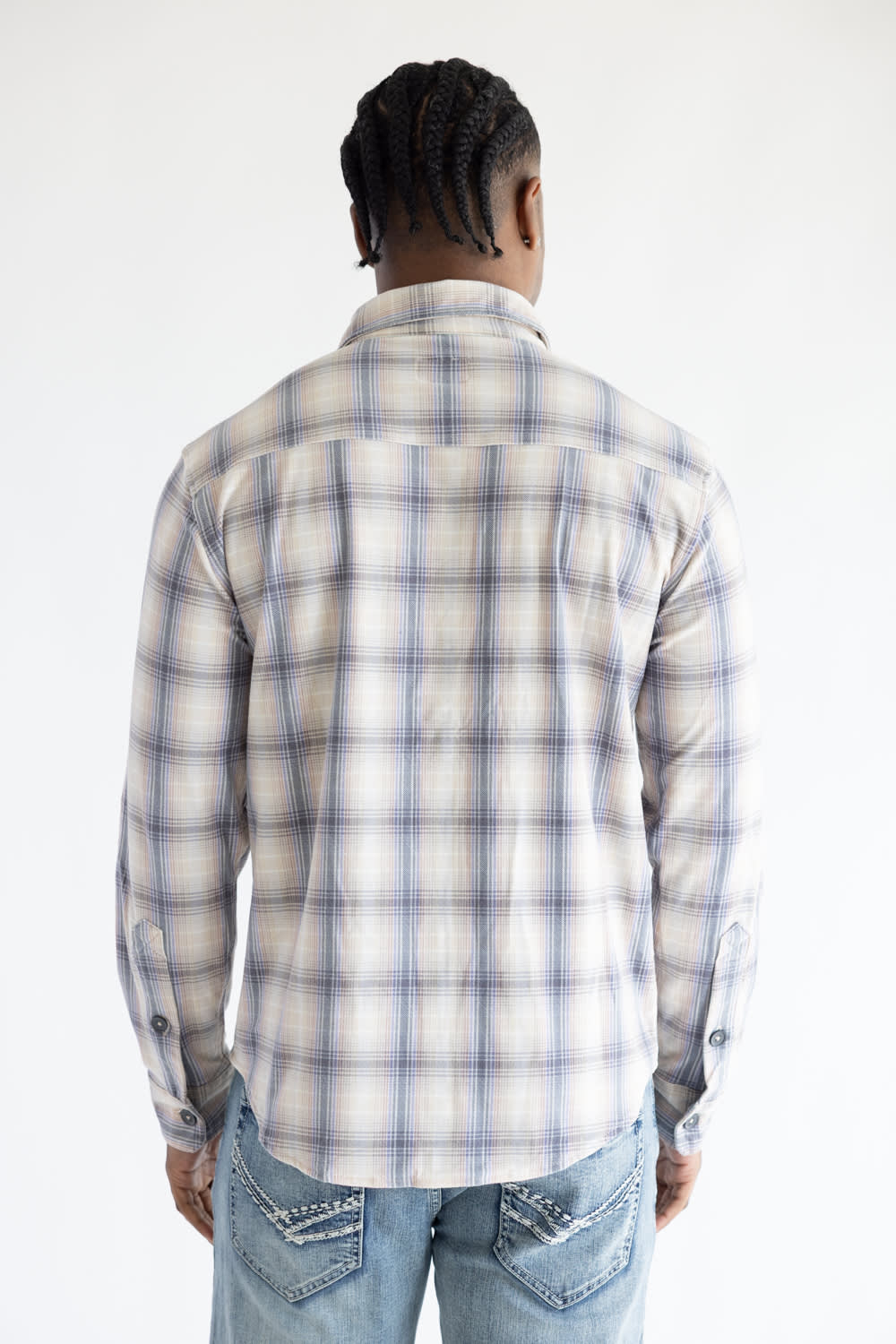 Back view of a man wearing the Hallstatt Knit Button Up Flannel Shirt in Sand with a plaid pattern in blue, beige, and gray, paired with light-wash jeans against a white backdrop