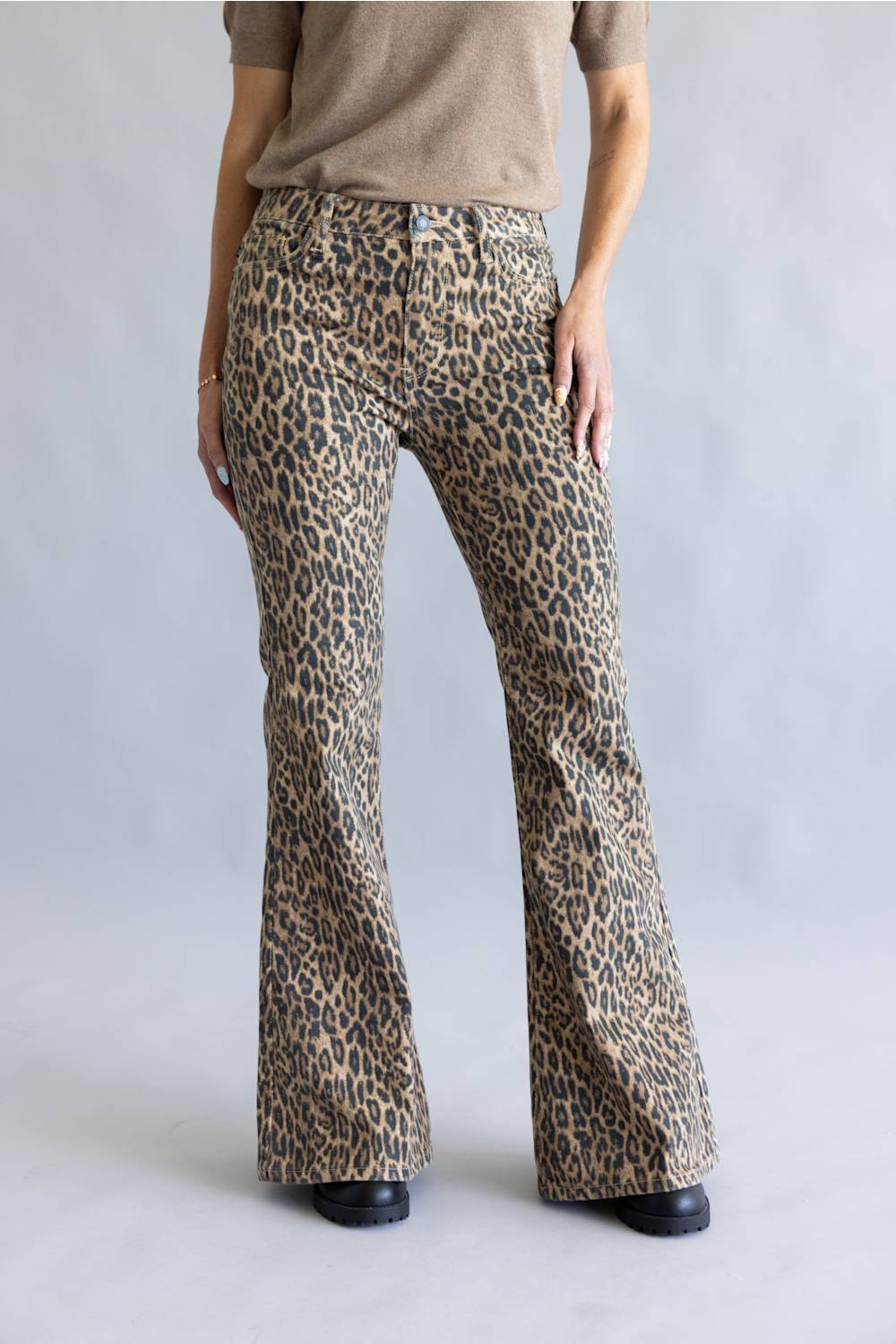 A person wearing leopard-print flare pants with a beige top, shown from the waist down against a light gray studio background.